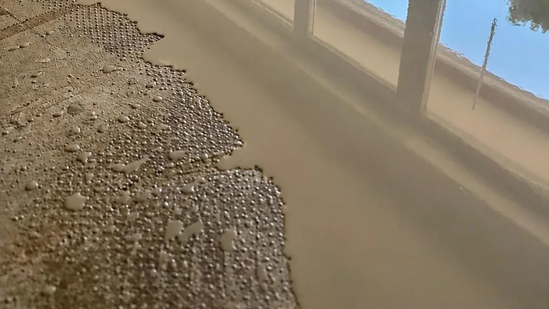 Frisch gegossene Ausgleichsmasse fließt über die Noppenplatte, die nasse Fläche spiegelt das Fenster