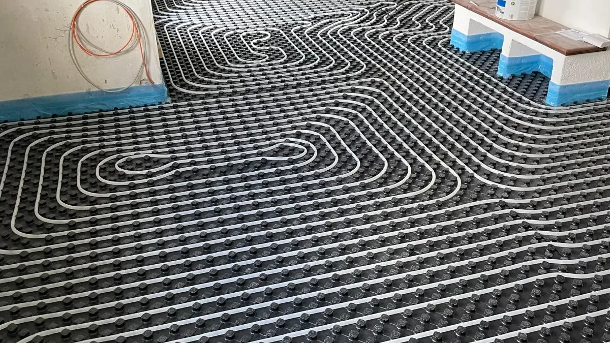 Vollflächig verlegtes Tackersystem: schwarze Noppenplatten mit eingelegtem weißem Heizrohr über die ganze Raumfläche