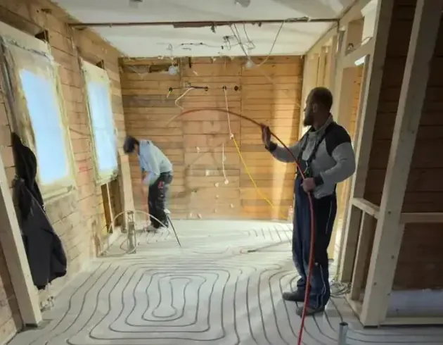 Zwei Monteure von Warmhome verlegen das Heizrohr auf dem frisch gefrästen Estrich im Rohbau